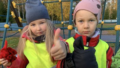 Alma och John deltar i försöket med tvåårig förskola. Här står de framför en klätterställning och visar tummen upp för sin förskola, Knattebo i Malax.
