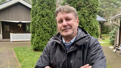 Mansantagen person står med armarna i kors i trädgård.