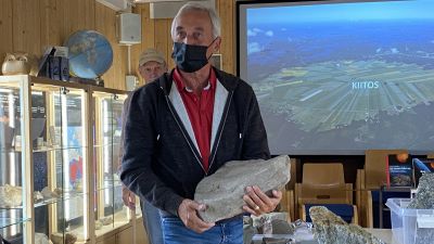 En man med munskydd står och håller i en sten med fossil från miljontals gamla kryp.