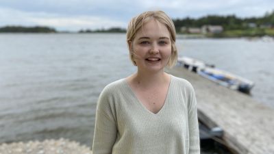 Ung kvinna vid vattenbrynet ler i en beige tröja.