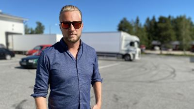 En ljushårig man i solglasögon står på en parkering.