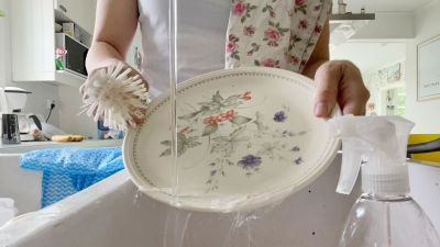 En kvinnas händer syns medan hon diskar ett blommigt fat i diskhon.