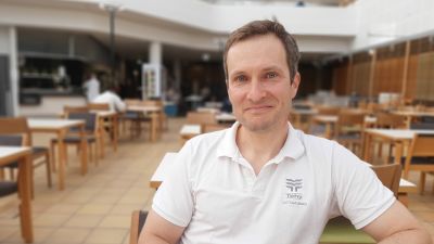 Eljas Honka-Hallila, en man med vit skjorta och mörkt hår, sitter i en stor matsal.