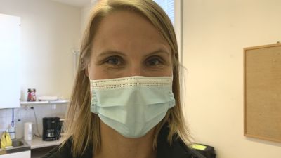 Kvinna med munskydd står i pausrum, i bakgrunden syns en köksbänk.