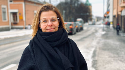 Kvinna i svart jacka och halsdukstår på en trottoar.
