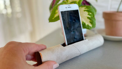 En tom hushållspappersrull ligger på bordet. Ett hål har klippts i rullen och där har en mobiltelefon placerats.