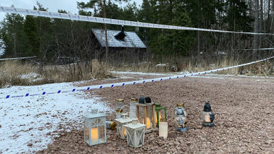 En stuga vars gård är avspärrad med polistejp, lyktor och gravljus på marken.