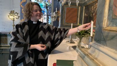 Kvinna tänder ljus i kyrka.