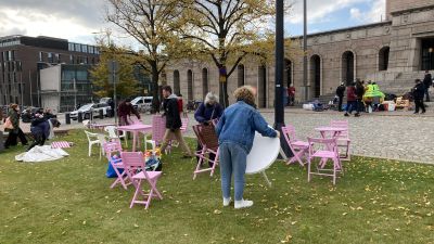 Personer ställer fram bord och stolar på en gräsplätt framför riksdagshuset.