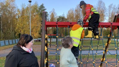 Förskolebarn klättrar i klätterställning medan två pedagoger tittar på.