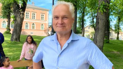 En glad äldre man står i en park och tittar leende in i kameran. Bakom honom syns en leende ung flicka samt en yngre lite fundersam flicka.