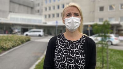 Medelålderskvinna med axellångt blont hår och munskydd tittar in i kameran.