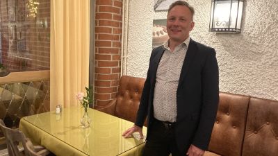 En man med blommig skjorta och blå kavaj ler mot kameran.