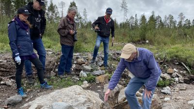 Fem personer står och tittar på en berggrund.