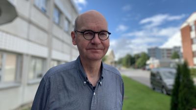 Mansperson står utomhus i sommargrönska.