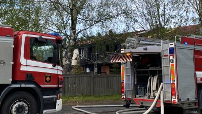 Ett tvåvåningsradhus som brunnit, av fyra lägenheter är de två mittersta förkolnade. I förgrunden syns två brandbilar.