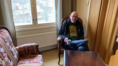 En man sitter i en fåtölj med en kaffekopp i handen.