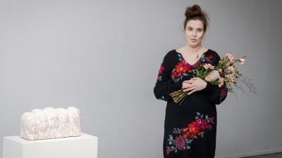 Emma Jääskeläinen står vid en skulptur och har en blombukett i händerna.