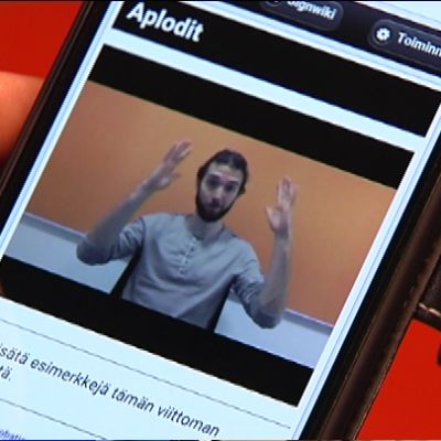 Signwiki kännykän näytöllä. Henkilö viittomassa termia "aplodit".