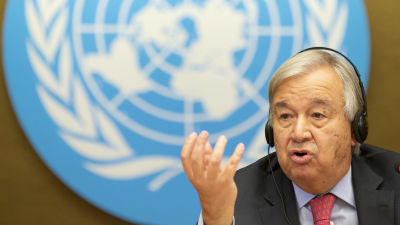 Antonio Guterres med handen i vädret, i bakgrunden FN-logon.