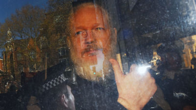Julian Assange näyttää peukaloa auton ikkunasta.