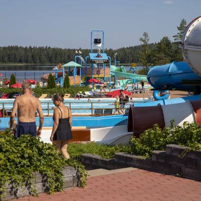 Kouvolan Tykkimäki Aquaparkissa pariskunta kävelee altaalle, taustalla altaita ja vesiliukumäkiä.