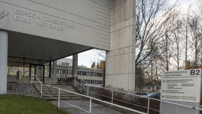 En modern byggnad som det står "Esbo rättshus" på. Huvuddörren och en trappa syns framför byggnaden.