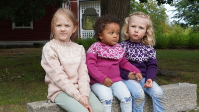 Tre barn sitter på en bänk iklädda strömsötröjor i barnstorlekar