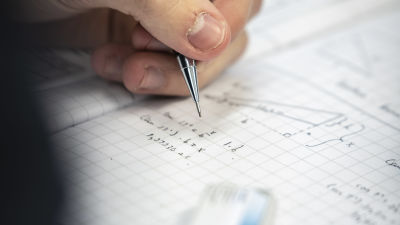 En studerande skriver matematiska formler i ett häfte.