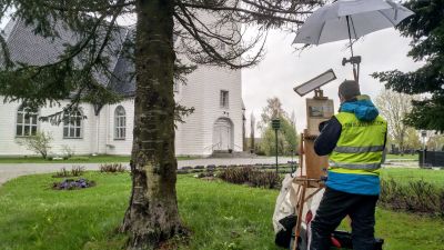 En konstnär står vid ett staffli och målar av en kyrka