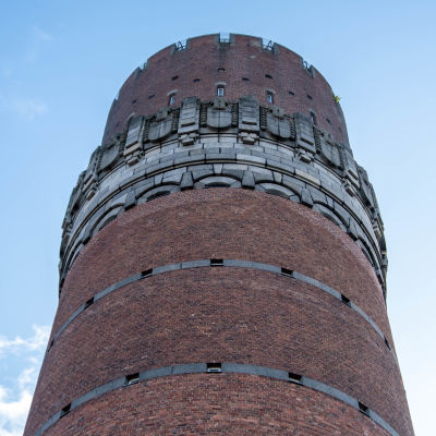 Runt torn i rödtegel, högst upp en stiliserad rand i gråfärgad sten.