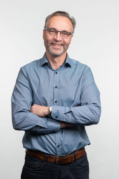 Skäggig glasögonförsedd man ler in i kameran.