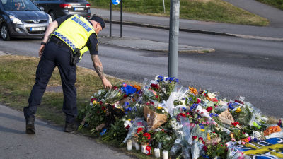 En polis lägger ner blommor vid en lyktstolpe där det samlats blombuketter.