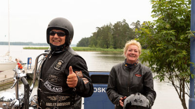 Två människor iklädda motorcykelkläder står vid strand.
