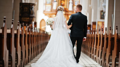 Ett brudpar går med ryggen till kameran längs mittgången i en kyrka.