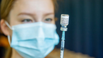 En person med ansiktsskydd förbereder ett coronavaccin.