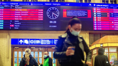 Människor på järnvägsstationen i Helsingfors. I bakgrunden syns ljustavlan med många inställda tåg.