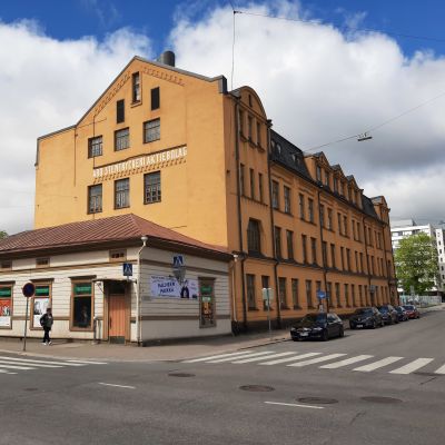 Åbo stentryckeri, en stor gul stenbyggnad i ett gathörn, med en liten ljus träbyggnad från 1821 framför sig.