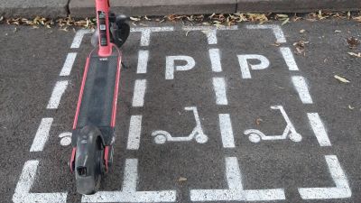 En orange elsparkcykel är parkerad i en ruta på gatan enkom för elsparkcyklar.