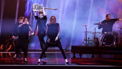 Blind Channel uppträder på eurovisionsscenen. Gitarristen håller upp baksidan av sin gitarr där det står "join".