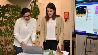 Två kvinnor står och jobbar och pratar vid en dator.