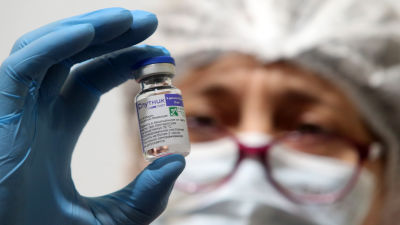 En sjukskötare i munskydd och glasögon håller upp en dos med Sputnik-vaccinet.