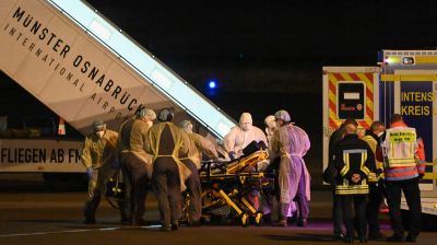 Medicinsk personal i skyddskläder och skyddsutrustning omger en bår med en patient som är på väg till en ambulans.