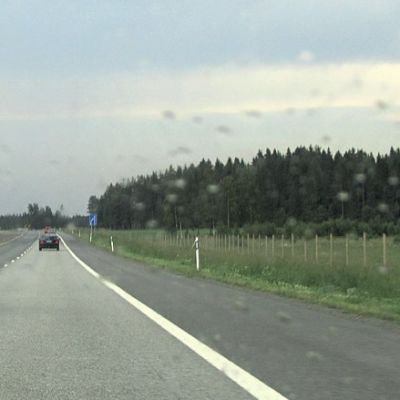 Punainen auto ajaa ohi ohituskaistalla. Kauempana edessä näkyy samaan suuntaan ajavia autoja.