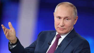 Vladimir Putin i närbild med huvudet på sned och höger handen utsträckt till sidan.