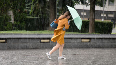 En kvinna i klänning går ute i regnet med ett paraply.