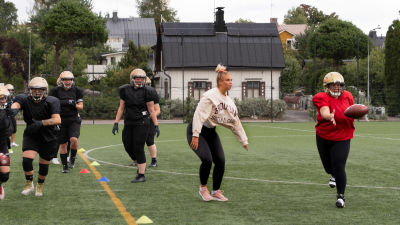 Kvinnor spelar amerikansk fotboll genom att en boll flyger och många spelare springer.