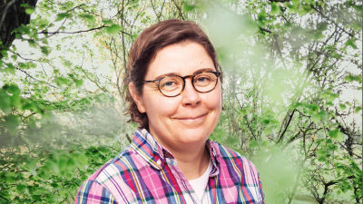 Bigo Lindholm småler in i kameran framför en grönskande bakgrund.