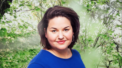 Daniela Franzell småler in i kameran framför en grönskande bakgrund.