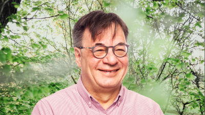 Kaj Martin småler in i kameran framför en grönskande bakgrund.